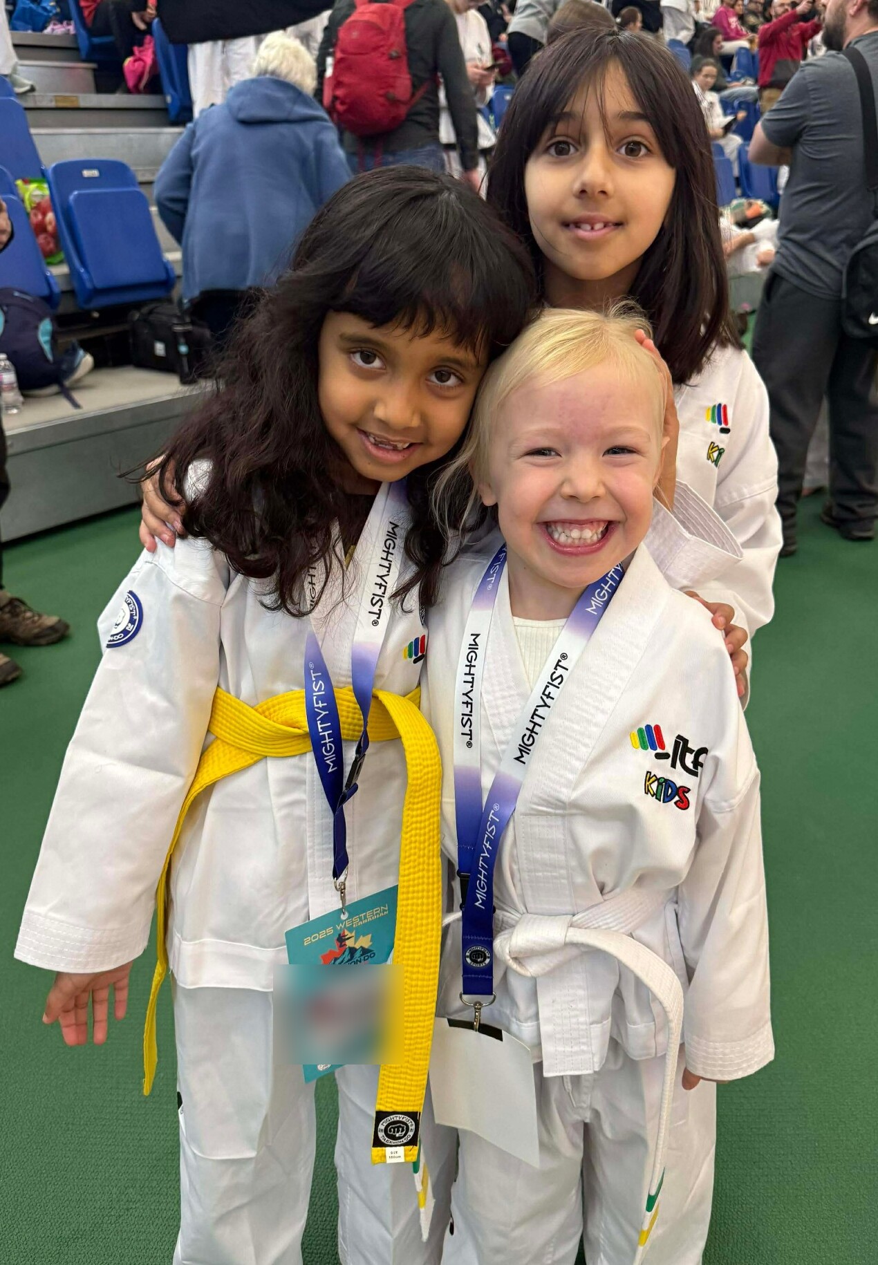 Three young Impact students smiling together with competition medals, with event badge details blurred