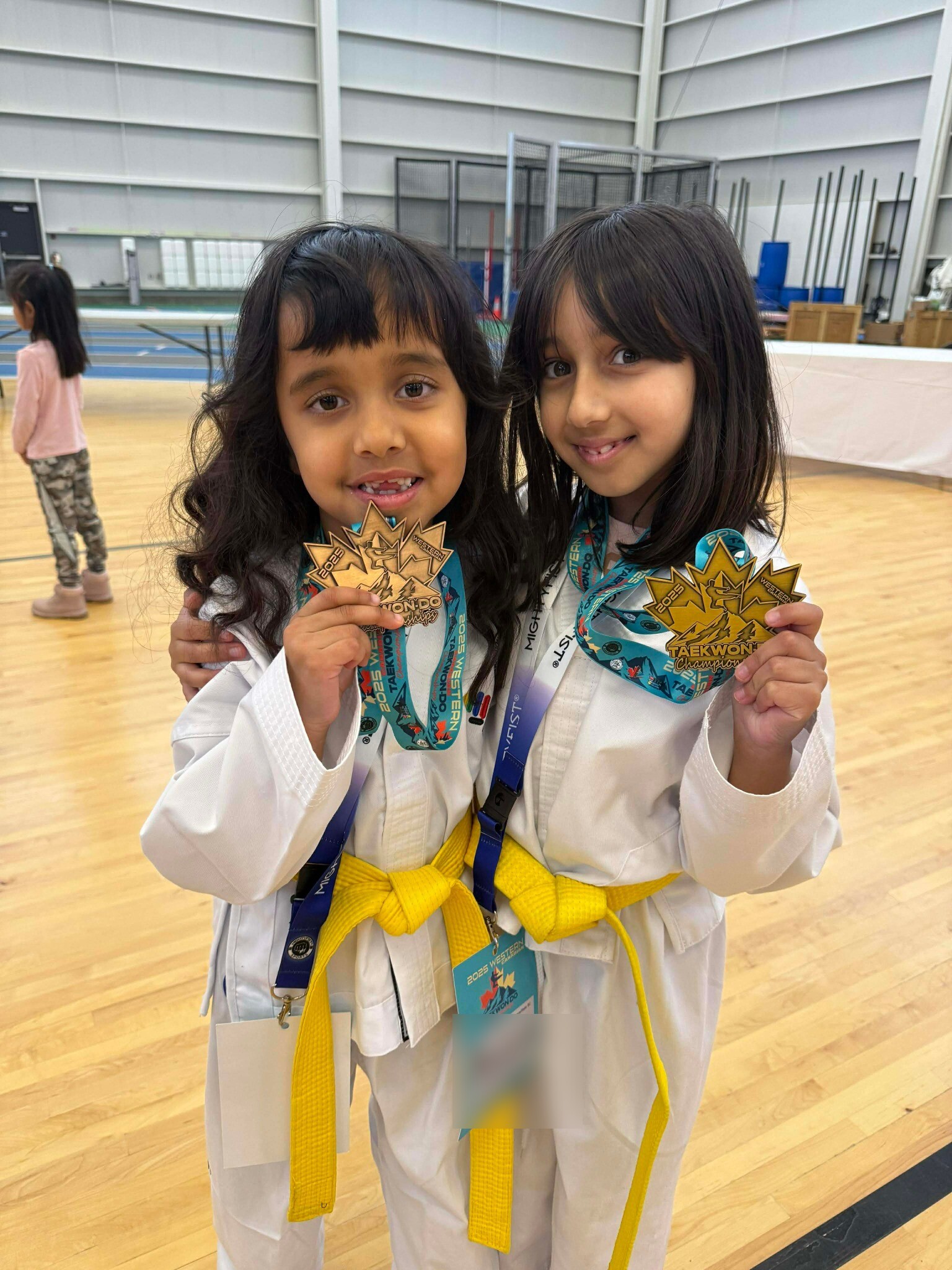 Two Impact students proudly showing their martial arts medals, with event badge details blurred